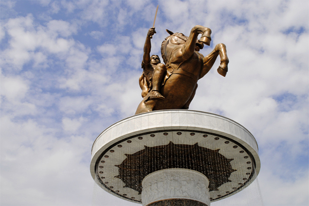 Bronze equestrian statue atop a fountain in Skopje, Macedonia under a cloudy sky.